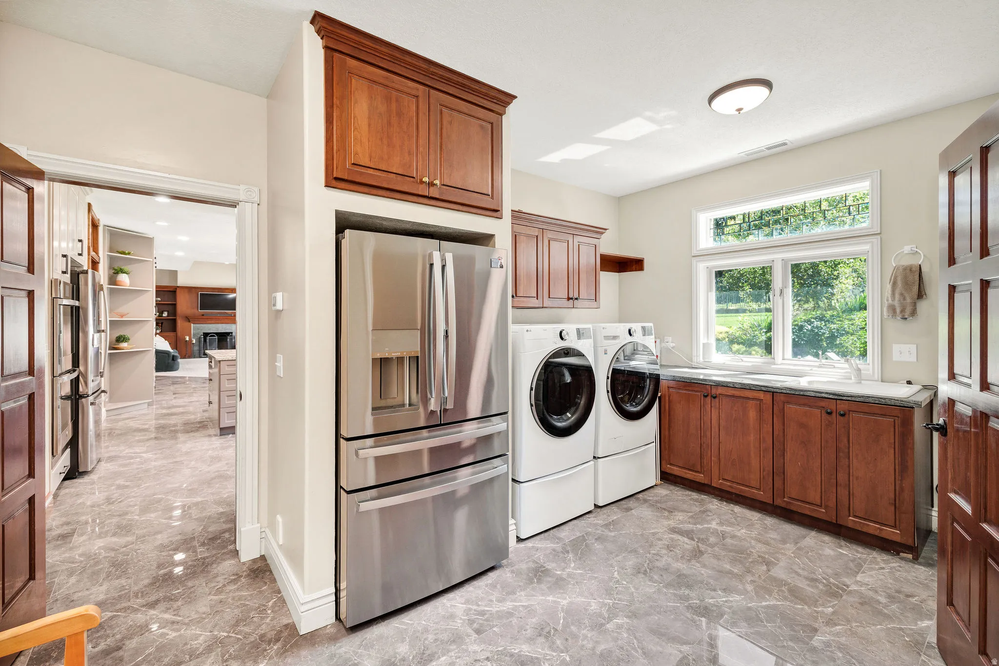 Polished marble-look flooring, wood-finish cabinetry, built-in stainless steel refrigerator, and dual windows