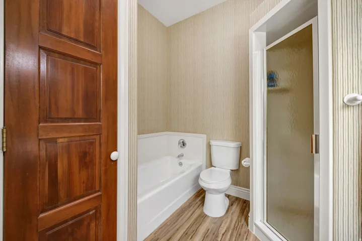 Wood-finish flooring, full-size bathtub, toilet, and shower enclosure with frosted glass