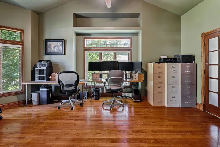 Wood-finish flooring, vaulted ceiling, multiple windows with blinds, wood trim throughout, and a wood-frame interior door with glass panels