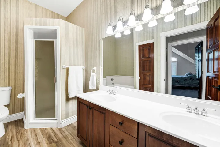 Dual vanity with white countertop, wood-finish flooring, stand-up shower, and vaulted ceiling
