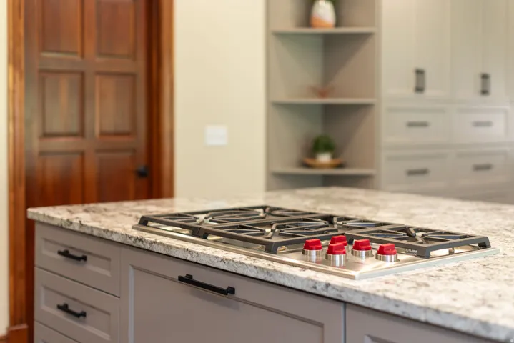 Chef's kitchen featuring a stainless steel gas cooktop with multiple burners, elegant light-filled countertops with subtle veining, soft-close cabinetry with integrated hardware, and open shelving with decorative accents