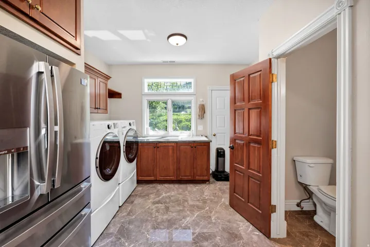 Laundry area featuring a side-by-side washer and dryer, wood-finish cabinetry, a stainless steel refrigerator, and marbled floor tile