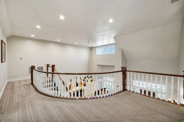 Carpeted loft space with a curved wooden banister and white spindles, recessed lighting, and a high ceiling