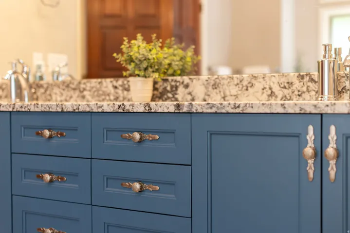 Vanity featuring blue cabinetry, patterned countertop, and decorative bronze hardware