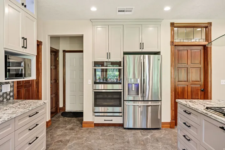 Kitchen featuring stainless steel appliances, built-in double oven, refrigerator, wood-finish base trim, and a decorative wood-frame transom window