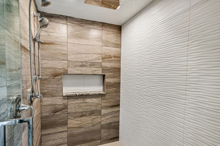 Walk-in shower with natural stone-look tiling, a textured accent wall, and a built-in shower niche with a granite-look shelf