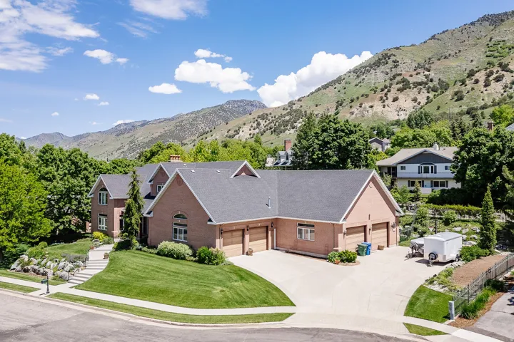 Brick exterior residence with a multi-car garage, mature landscaping, paved driveway, and mountain scenery