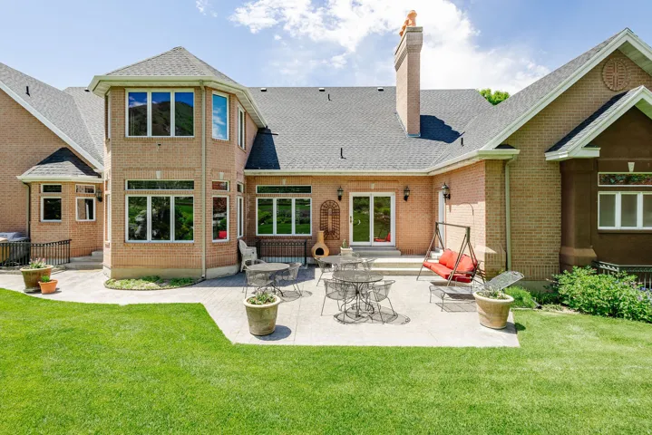 Expansive backyard featuring a manicured lawn, a large paver patio, brick exterior, multiple windows, and sliding glass doors