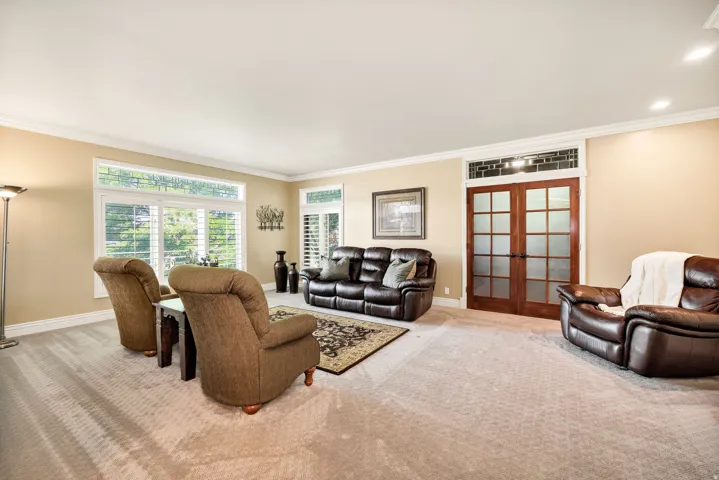 Recessed lighting, wood-frame double doors with frosted glass panels, transom window with intricate detailing, large windows with plantation shutters, and crown molding