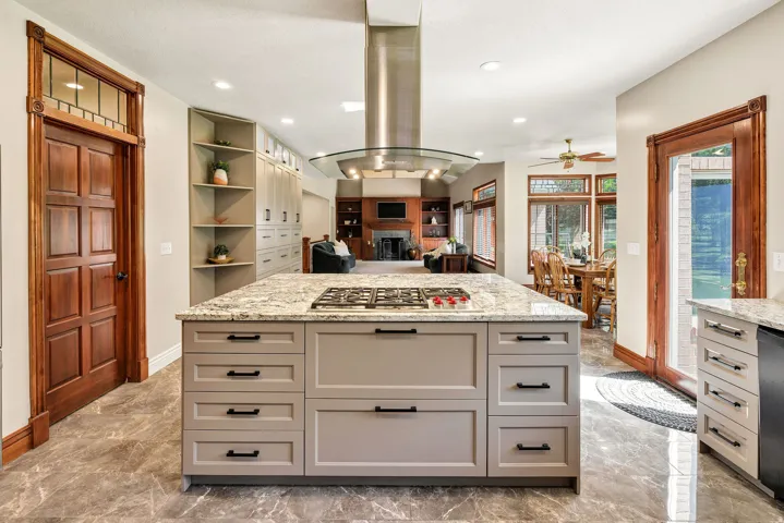 Kitchen featuring a large island with a cooktop, granite countertops, an overhead range hood, extensive built-in cabinetry, and tile flooring