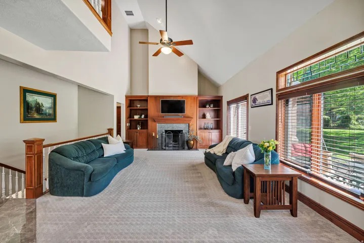 Vaulted ceilings with a ceiling fan, built-in cabinetry, a fireplace with a stone surround, and large windows with transom details