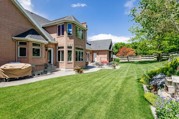 Expansive backyard featuring a manicured lawn, established landscaping, and a brick exterior with multiple windows