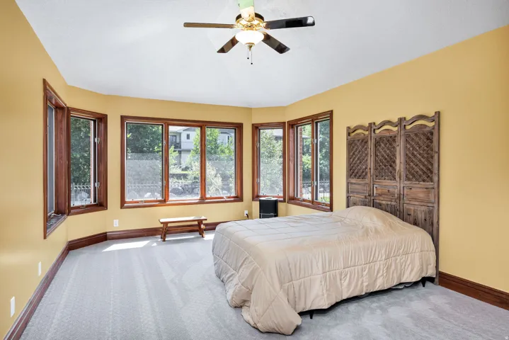 Curved wall with multiple windows, light-colored carpeting, wood-finish trim, and a ceiling fan with integrated lighting