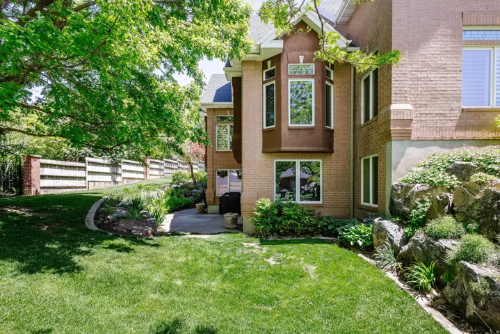 Brick exterior with a bay window, a paved patio, and a sloped lawn with rock landscaping