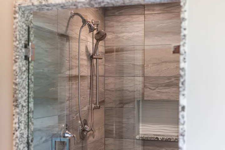 Glass-enclosed shower with a brushed nickel shower system, full-height tile surround, built-in niche, and granite-finish threshold