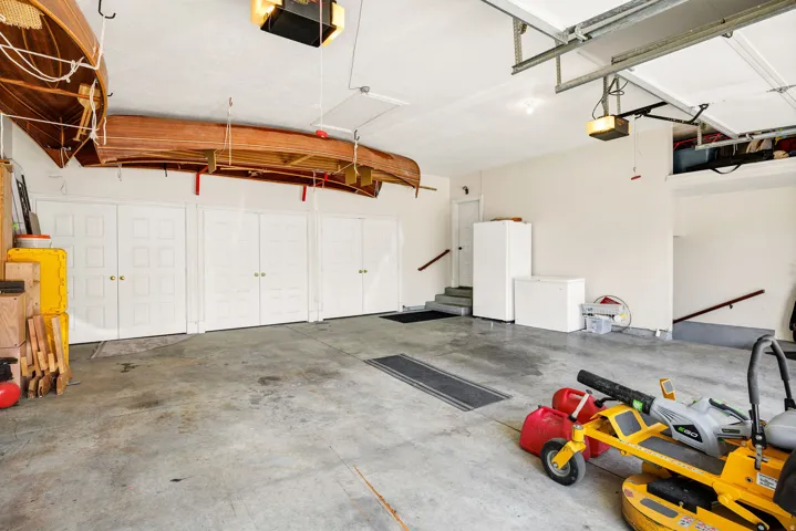 Attached garage with concrete flooring, multiple built-in storage cabinets, and stairs providing access to additional levels