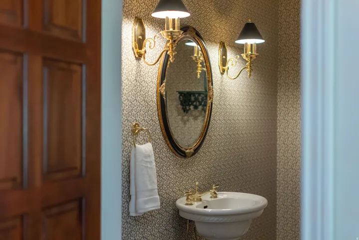 Pedestal sink with brass-finish hardware, oval framed mirror, and two wall sconces with black shades