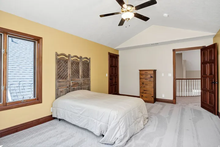 Vaulted ceiling with a ceiling fan, wood-framed windows, and hardwood doors