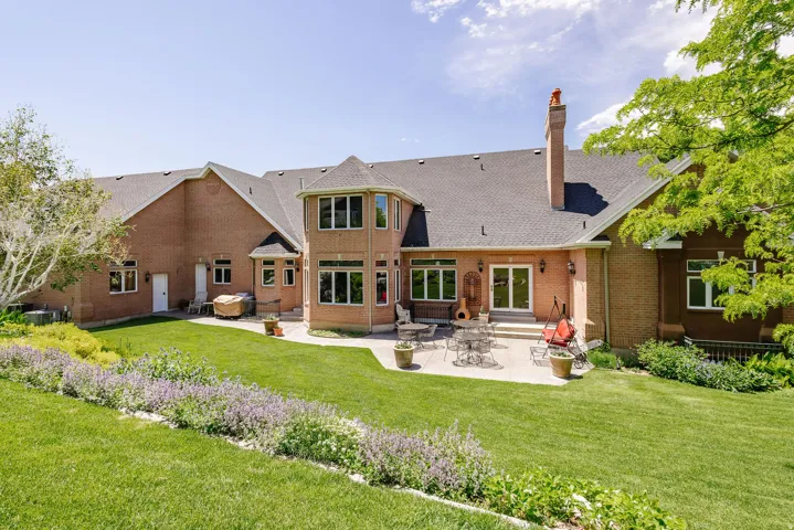 Expansive rear facade featuring brick construction, a multi-level roofline, a tiered concrete patio, and a landscaped lawn