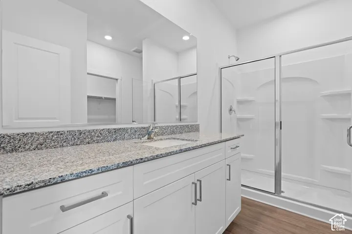 White shaker-style cabinetry, a spacious vanity with a light-toned stone countertop, an integrated sink, a large wall mirror, and a glass-enclosed shower with built-in shelving