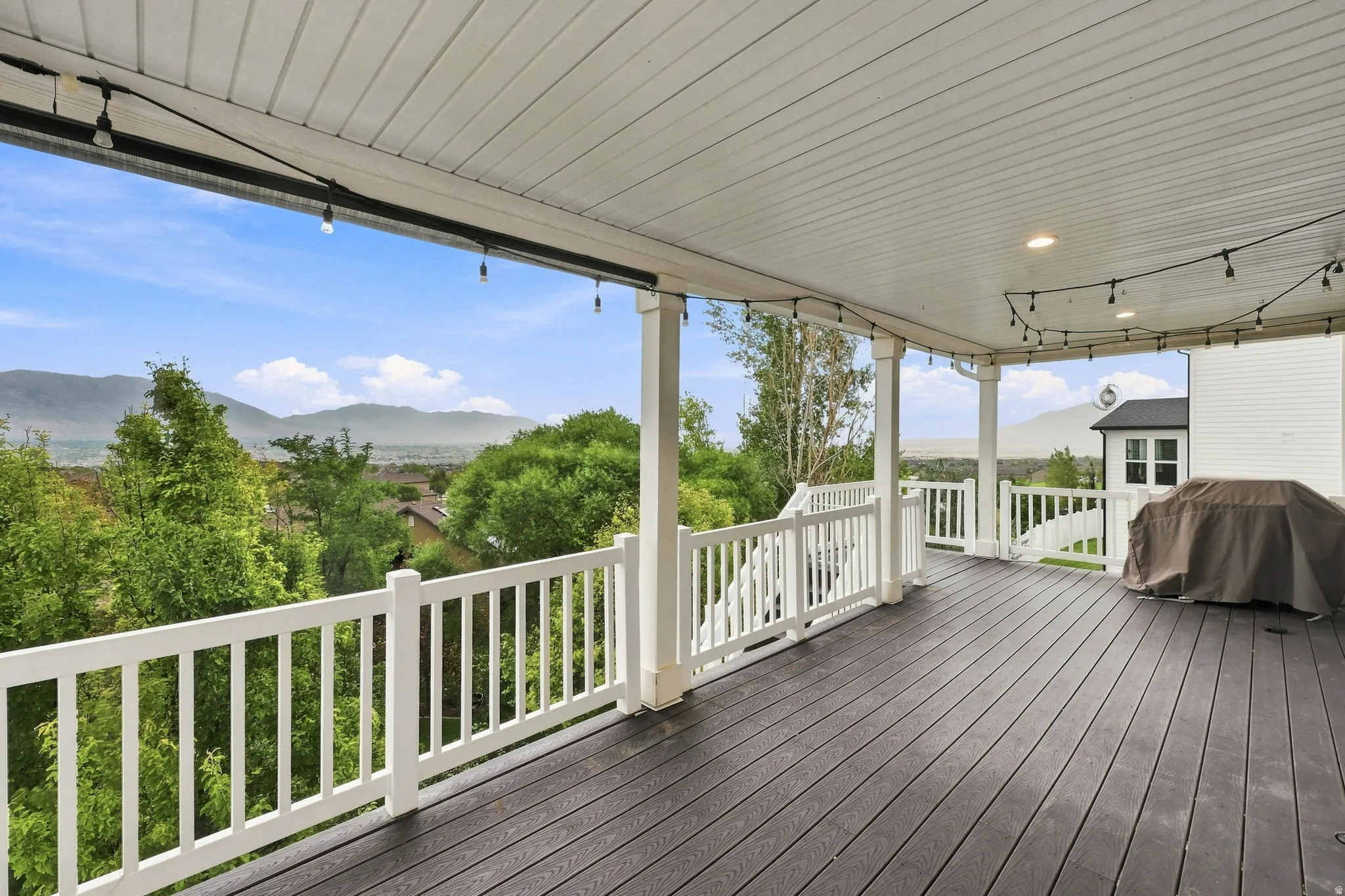 Spacious covered deck featuring dark wood-finish decking, white railings, and recessed ceiling lighting