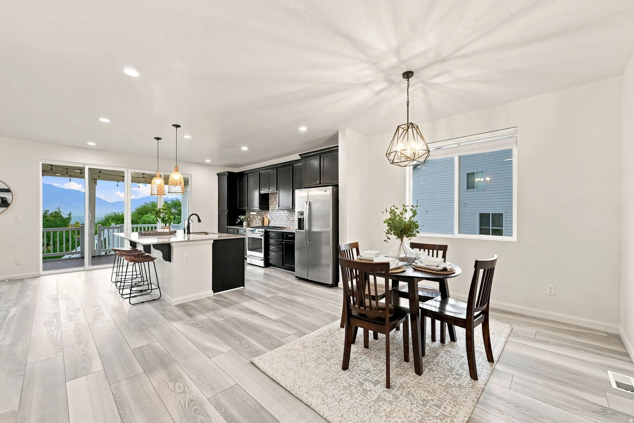 Open-concept design featuring wood-finish flooring, a kitchen island with seating, dark cabinetry, and sliding glass doors leading to an outdoor deck