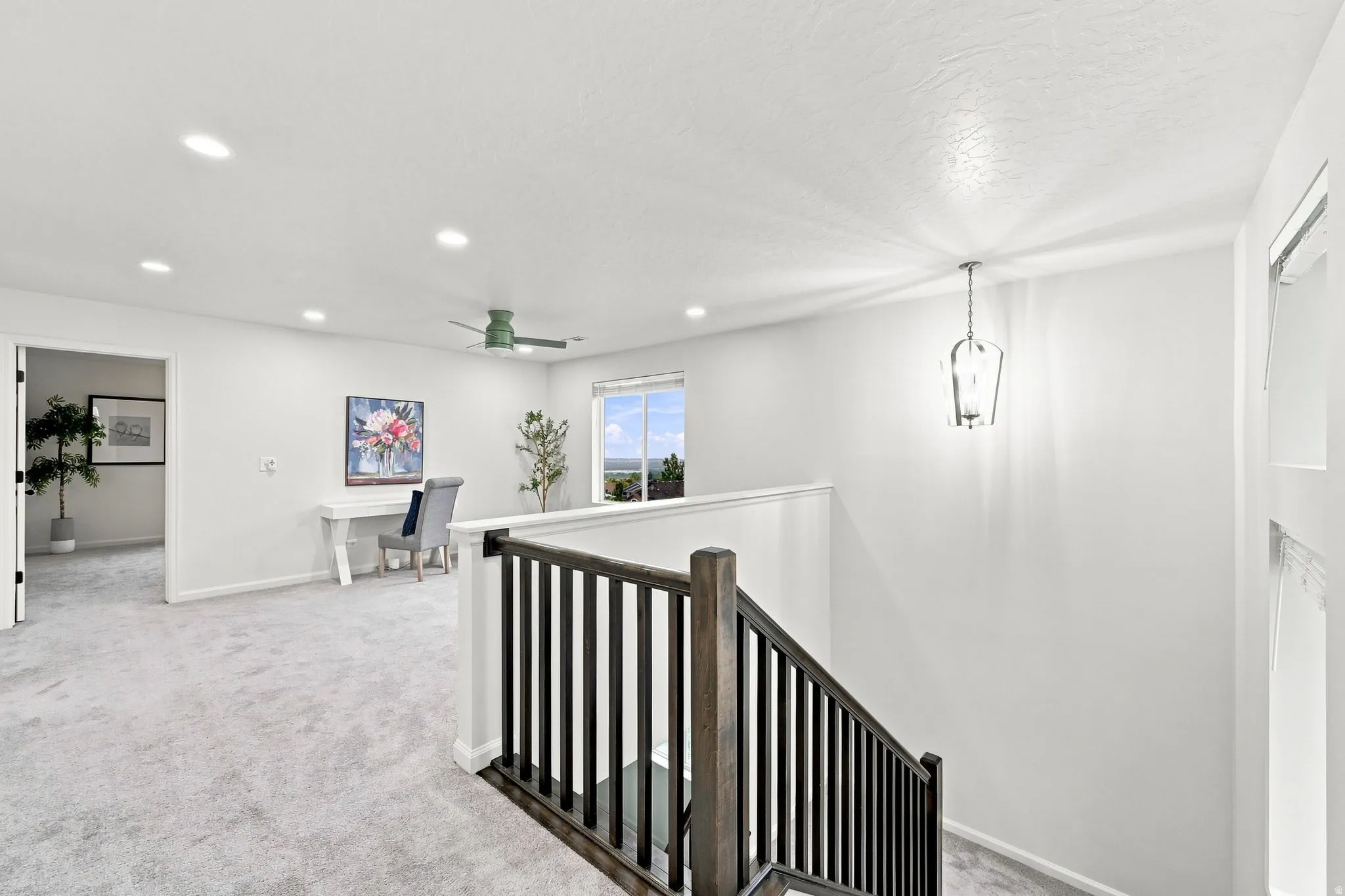 Expansive open landing with recessed lighting, a ceiling fan, and a chandelier, featuring a dark wood newel post and balusters