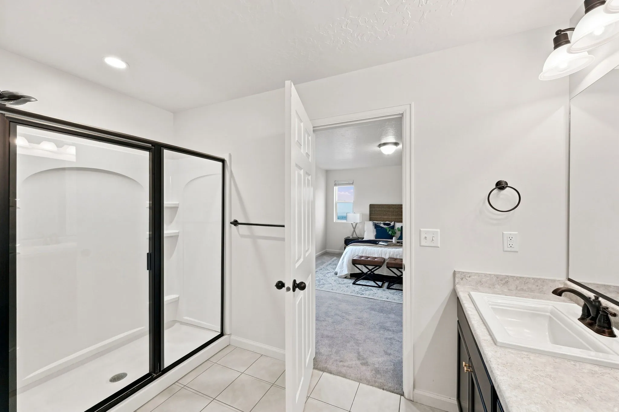 Walk-in shower with black-framed glass enclosure, single vanity with integrated sink, black hardware, and light-toned countertop