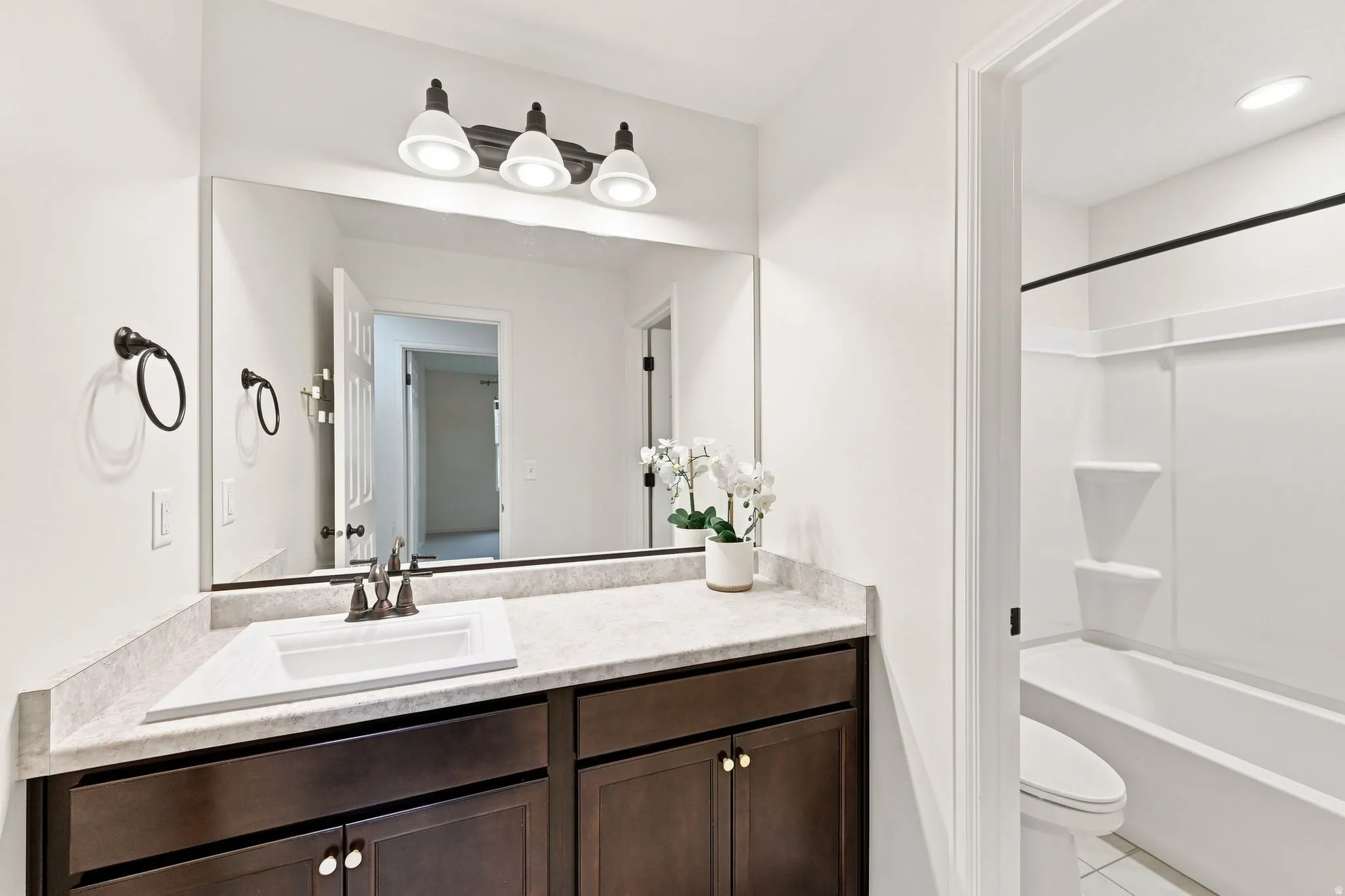 White vanity with dark wood-finish cabinetry, integrated sink, and bronze-finish fixtures