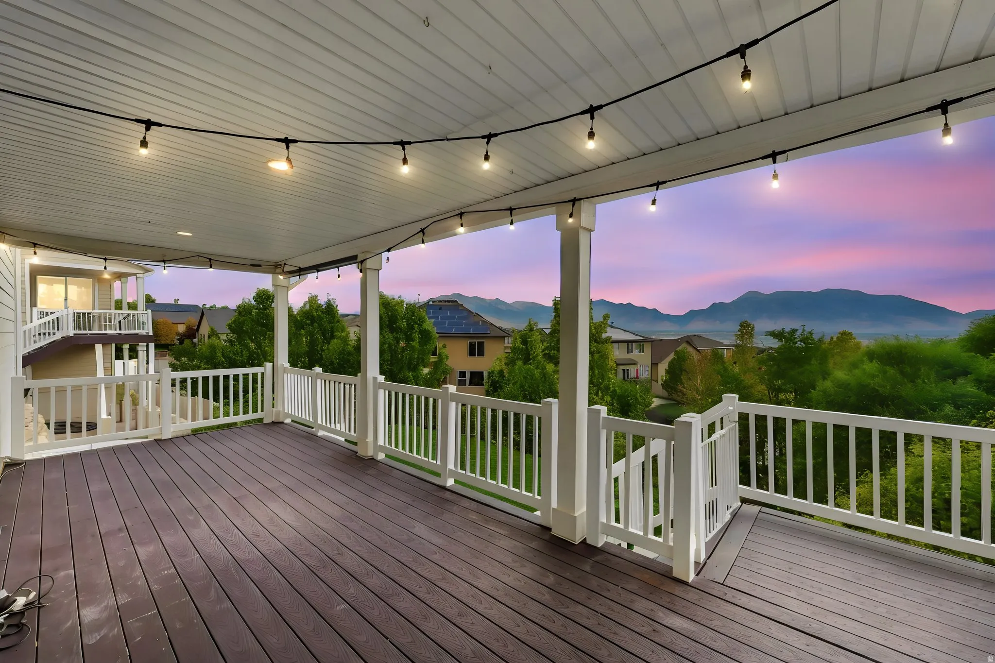 Covered deck with dark wood-finish flooring, white railing, and string lighting