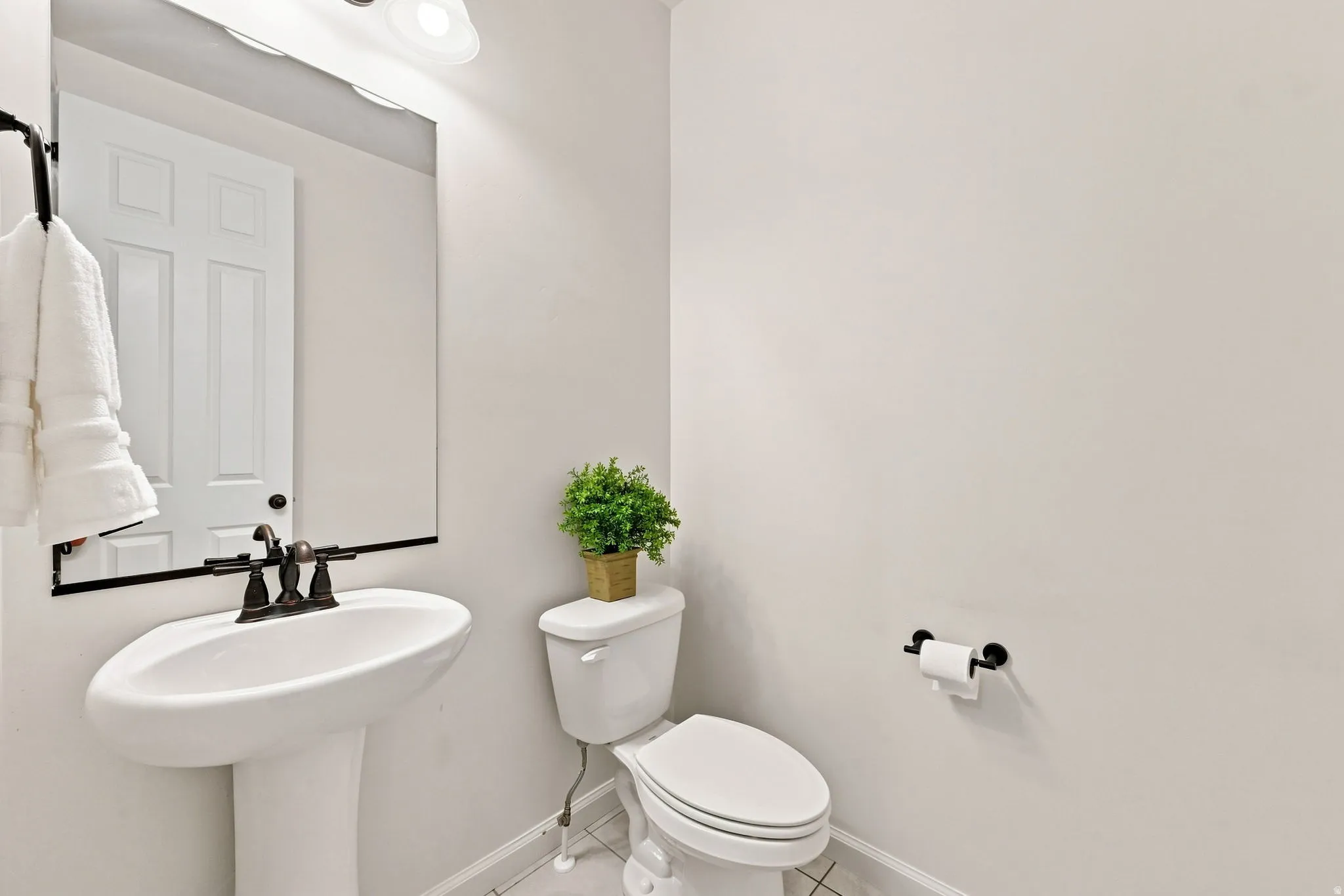 Powder room featuring a pedestal sink with oil-rubbed bronze faucet, framed mirror with integrated lighting, white porcelain toilet, and neutral wall finishes