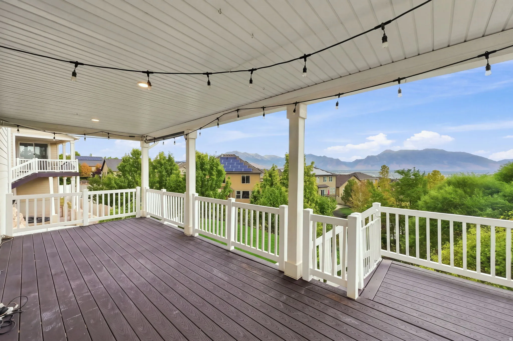 Expansive covered deck with dark wood-finish flooring, white railing, and decorative string lighting