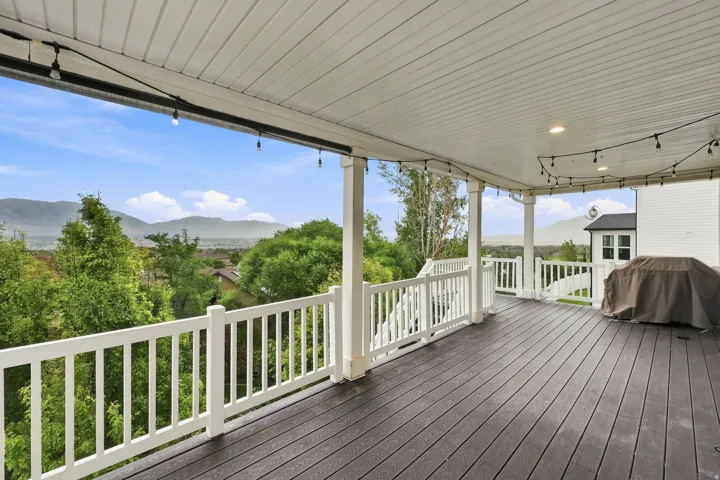Spacious covered deck featuring dark wood-finish decking, white railings, and recessed ceiling lighting
