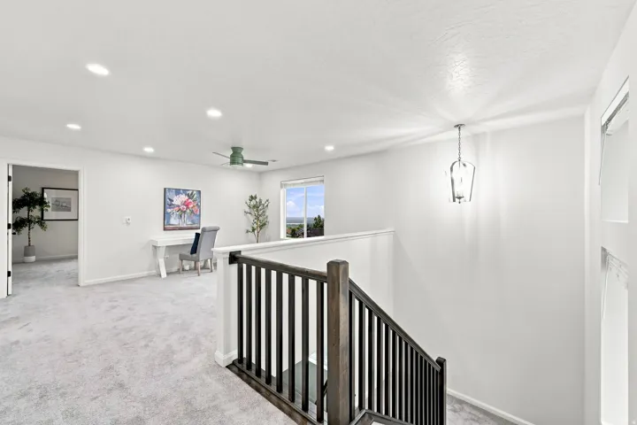Expansive open landing with recessed lighting, a ceiling fan, and a chandelier, featuring a dark wood newel post and balusters