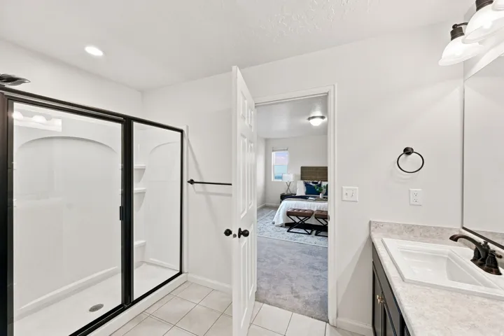 Walk-in shower with black-framed glass enclosure, single vanity with integrated sink, black hardware, and light-toned countertop