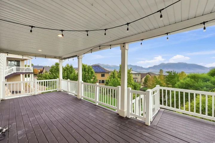 Expansive covered deck with dark wood-finish flooring, white railing, and decorative string lighting