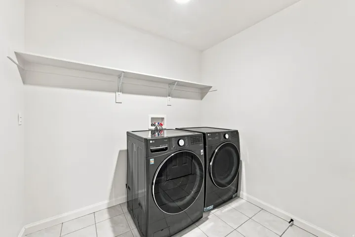 Integrated laundry area featuring neutral wall paint, tiled flooring, overhead shelving, and existing appliance connections
