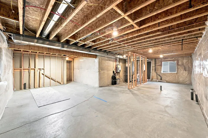 Unfinished basement with exposed ceiling joists, concrete flooring, and framed interior walls