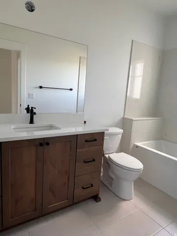 Wood-finish vanity with a white countertop and integrated sink, matte black faucet, and a large wall-mounted mirror
