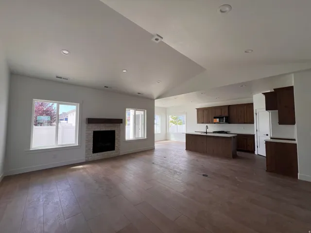 Vaulted ceilings with recessed lighting, wood-finish flooring, and a fireplace featuring a stone surround and wood mantle
