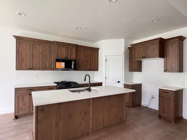 Kitchen featuring a central island, wood-finish cabinetry, light-toned countertops, white subway tile backsplash, and recessed lighting