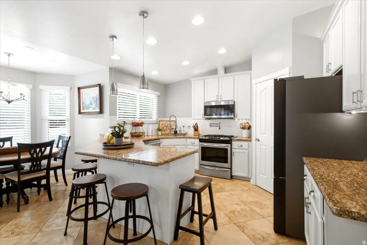 Kitchen featuring white shaker cabinetry, stainless steel appliances, a multi-tone tile backsplash, and an island with a quartz-finish countertop