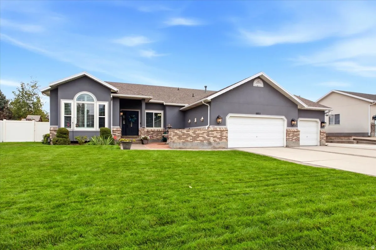 Stucco exterior with brick detailing, arched window, attached two-car garage, and a white privacy fence