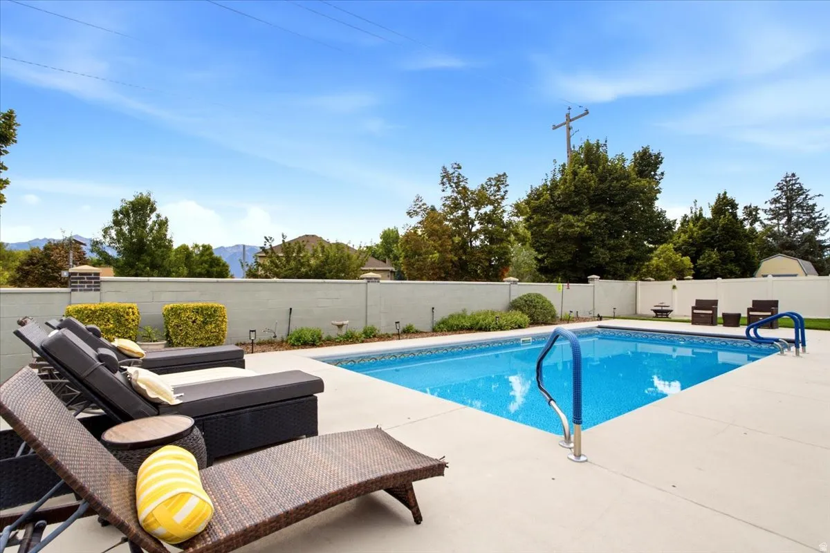 Outdoor swimming pool with concrete decking, blue-tiled interior, and perimeter fencing