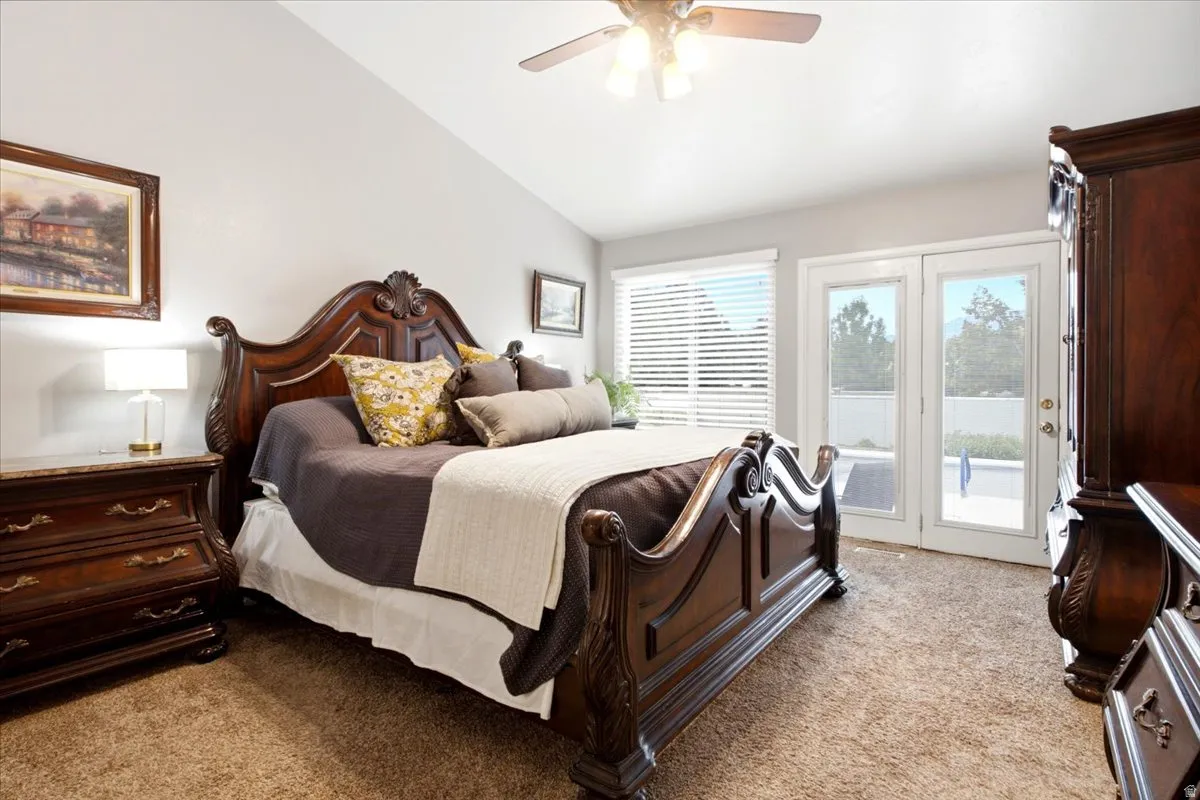 Vaulted ceiling with a ceiling fan, dual French doors, large window with blinds, and carpeted flooring