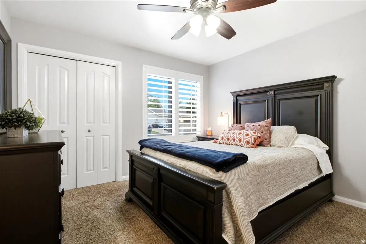 Neutral paint palette, ceiling fan, carpet flooring, window with plantation shutters, and bi-fold closet doors