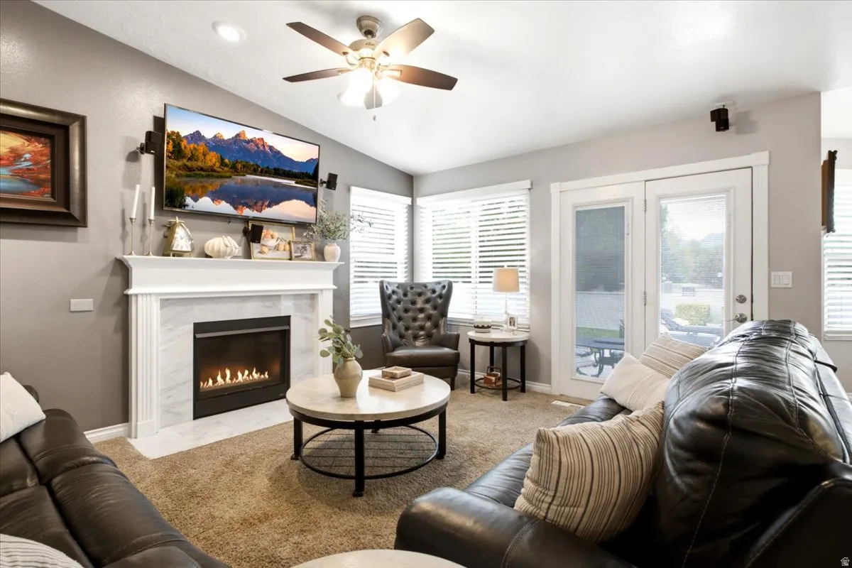 Living space featuring a white mantel fireplace with a dark surround, dual pane glass French doors, vaulted ceiling, and a ceiling fan