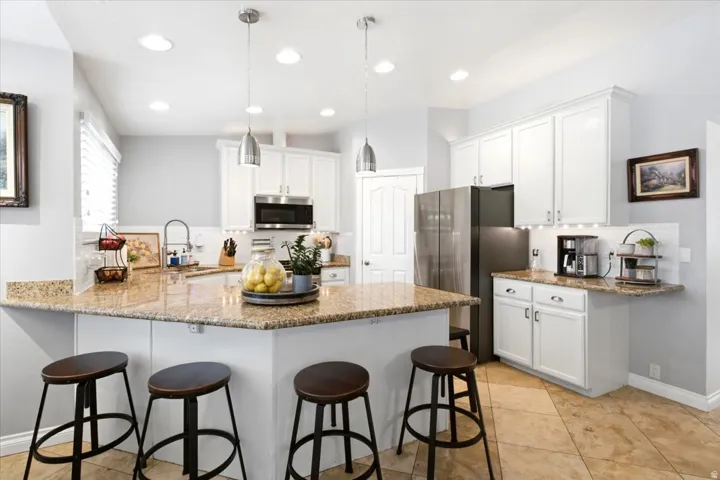 Quartz countertops, white shaker cabinetry, stainless steel appliances, recessed lighting, and tile flooring