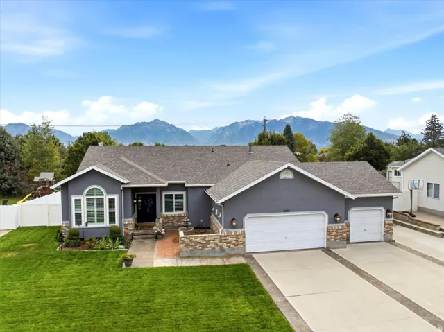Stucco exterior with stone accents, mature landscaping, a multi-car garage, and a paver driveway