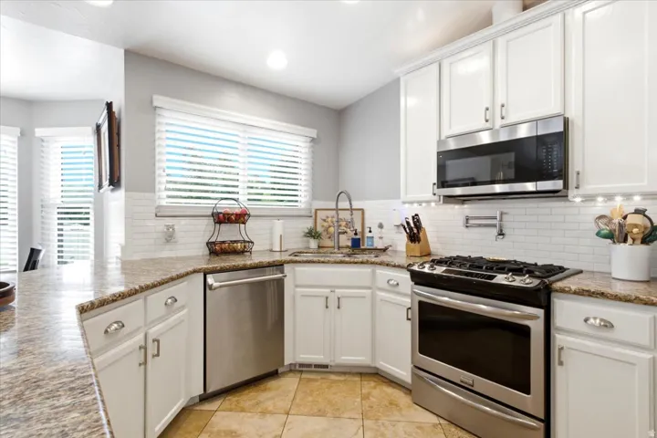 Kitchen featuring white cabinetry, undermount sink, stainless steel appliances, tile backsplash, and stone-finish countertops